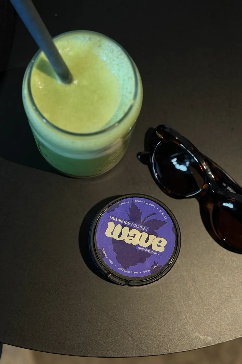 Puk WAVE na tmavém stole vedle zeleného smoothie a slunečních brýlí