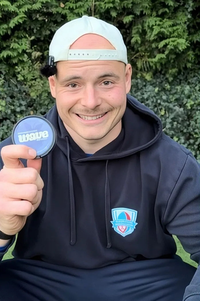 Usměvavý muž v bílé kšiltovce drží v ruce puk WAVE